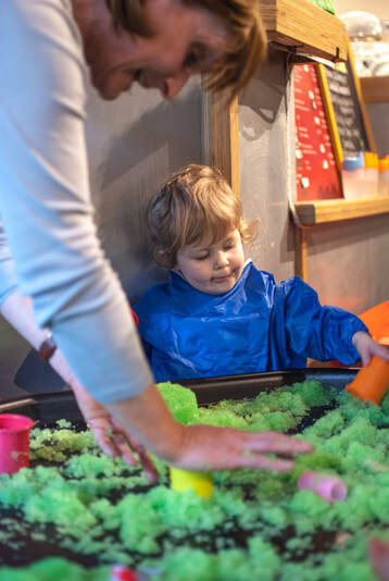Green slime and a young child and adult playing with it with their hands